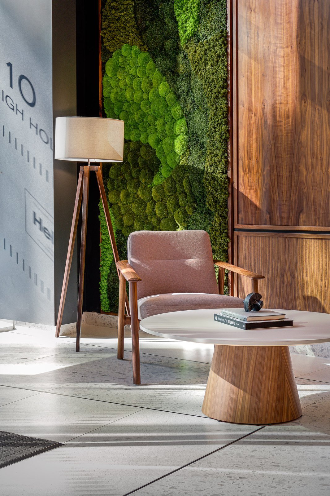 Walnut-framed lounge chair and round coffee table against a preserved moss wall in a reception lounge