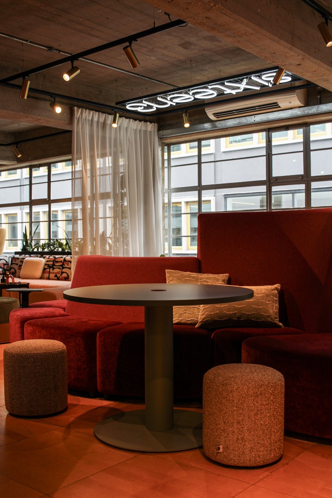 Sixteen3 breakout lounge with deep red modular seating, poseur table and upholstered stools